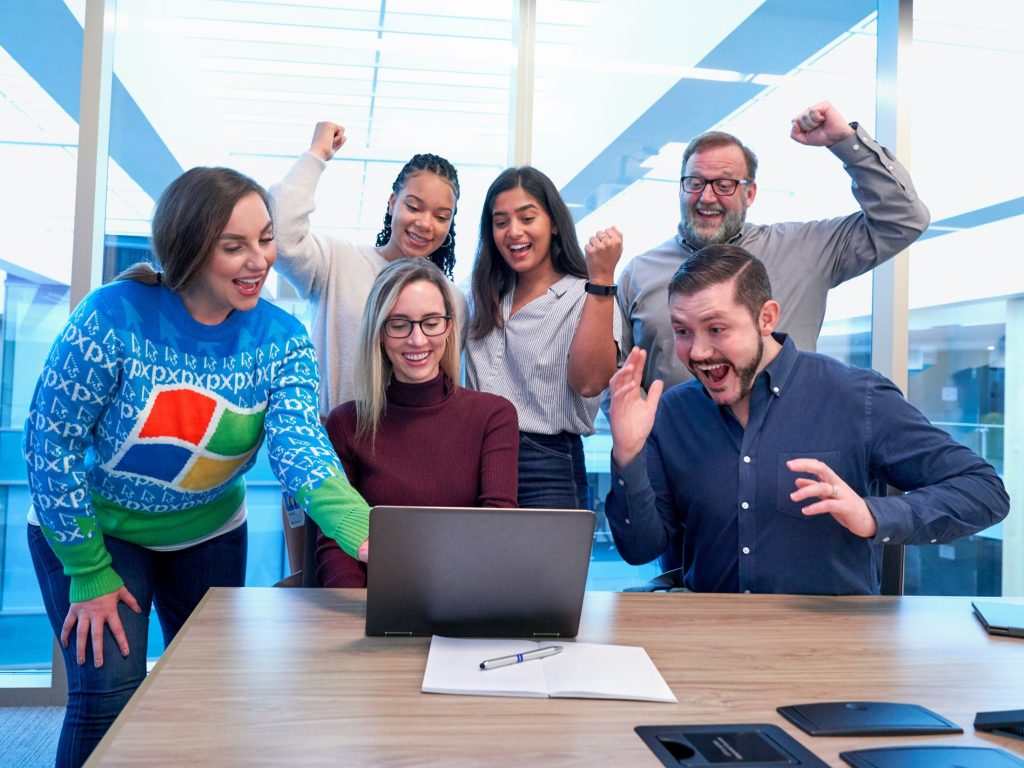Happy team around a laptop computer as navigating workforce anxiety remains a primary challenge for leaders as AI integration defines modern enterprise success.